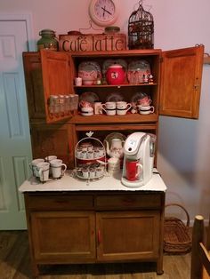 an old fashioned coffee maker on top of a wooden cabinet with cups and mugs