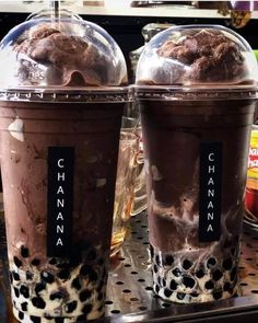 two ice cream sundaes with chocolate topping in plastic cups on a shelf next to each other