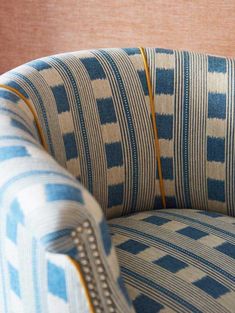 a blue and white striped chair with gold piping on the arm rests against a pink wall