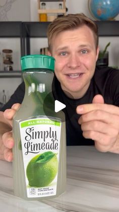 a man holding up a bottle of simply limeade on top of a white counter