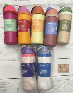 six different colored coffee mugs in plastic bags on a white wooden table with labels