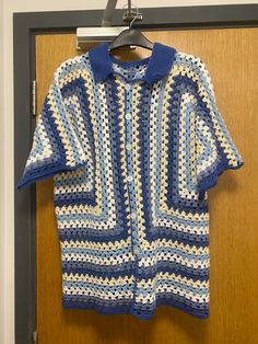 a blue and white crocheted sweater hanging on a door hanger with a wooden door in the background