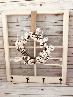 a wreath hanging on the side of a window in front of a white wooden wall