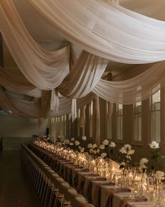 a long table with candles and flowers in vases on top of it, surrounded by white draping