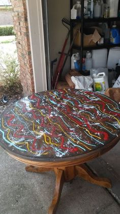 an old table has been decorated with colorful chalk paint and is sitting in front of a garage door