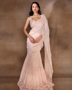 Blush pink tiered skirt with an attached drape hand embellished with ivory pearl drops & glass beaded lines. Paired with a hand embellished pearl & glass bead heavily hand embellished sweetheart neck blouse with beaded hanging tassels.From Shloka Khialani's Winter Sun collection.DELIVERY TIMEPlease allow 6-8 weeks for your outfit to arrive.FABRIC DETAILSGeorgette, Net, CrepeProfessional cleaning only. Elegant Wedding Gown With Tiered Skirt, Embellished Tiered Skirt Dress For Reception, Elegant Peach Georgette Lehenga, Elegant Peach Dress For Festive Occasions, Festive Embellished Tiered Skirt Dresses, Elegant Embellished Tiered Skirt Dress, Elegant Tiered Lehenga With Ruffles, Elegant Tiered Ruffle Lehenga, Elegant Festive Dress With Tiered Skirt