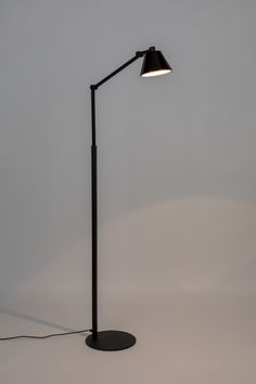 a black floor lamp with a white light on the side and a gray wall behind it