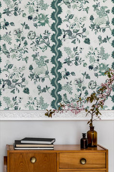 a wooden dresser sitting in front of a wall with a flowered design on it