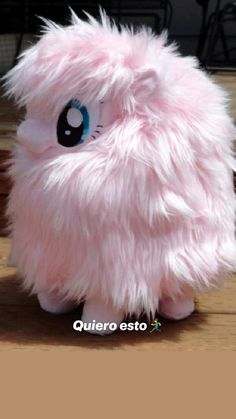 a pink stuffed animal with blue eyes sitting on top of a wooden table