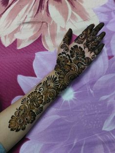 a woman's hand with henna on it and purple flowers in the background