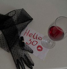 a glass of red wine next to a black dotted glove with the word hello 30 written on it