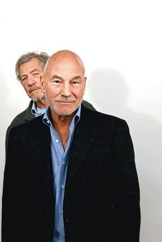 two men standing next to each other in front of a white wall with one man looking at the camera