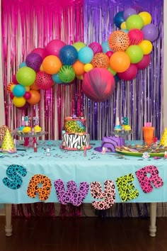 a party table set up with balloons, streamers and cake for an animal themed birthday