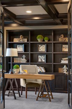 a home office with built - in bookcases and a wooden desk topped with a lamp