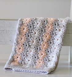 a crocheted blanket sitting on top of a wooden bench next to a white chair