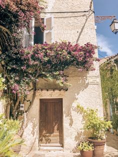 an old building with potted plants and flowers on the outside, next to a wooden door