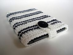 a crocheted cell phone case with a black button on the front and white stripes