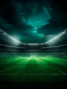 an empty soccer stadium at night with the lights on and dark clouds in the sky