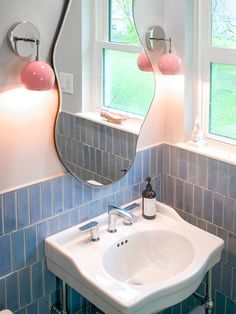 a white sink sitting under a bathroom mirror next to a window with two pink lights on it