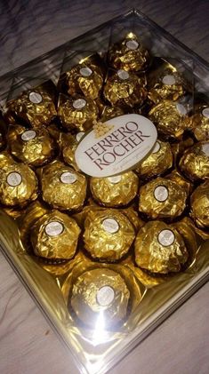 a glass box filled with gold foiled chocolates on a white cloth covered table