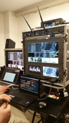 two laptops are sitting on a table in front of a television set with multiple monitors