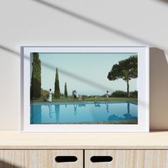 a framed photograph sitting on top of a wooden dresser next to a pool with people in it