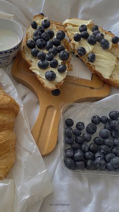 blueberries and croissants are on the table next to milk, butter and bread