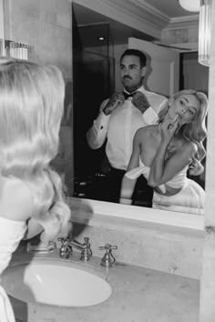 a man is brushing his teeth in front of a mirror while a woman looks at him