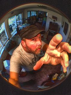 a man holding a cat in his right hand and looking at the camera through a fisheye lens