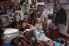 a woman laying in her bed surrounded by posters and other things on the wall behind her