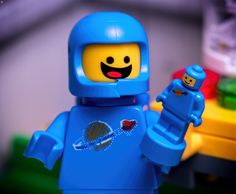 a lego man with a blue space suit holding a red object in his right hand