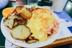 a white plate topped with potatoes and meat covered in gravy next to an orange slice