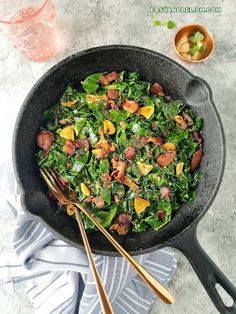 a skillet filled with spinach and bacon on top of a blue towel next to two gold utensils