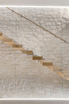 a wooden stair case in front of a white brick wall with glass railing and handrails