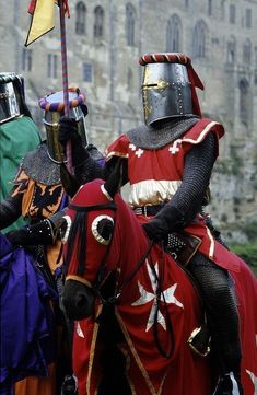 two knights in full armor on horseback with one holding a flag and the other standing behind them