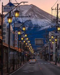 a car driving down an empty street in front of a snow covered mountain at dusk