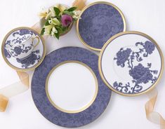 blue and white plates with gold rims are on a table next to a flower vase