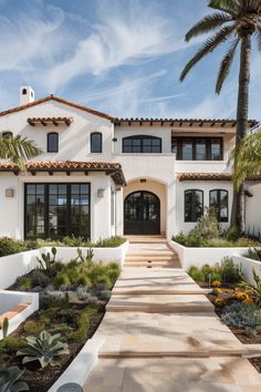 a large white house with lots of plants in front of it and palm trees on the other side