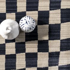 two white vases sitting on top of a checkered rug