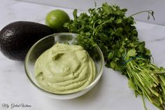 an avocado, cilantro and limes on a marble counter top