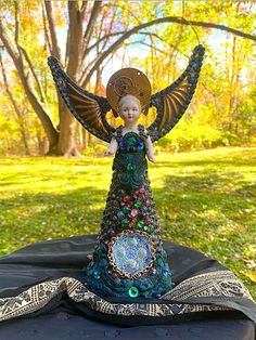 an angel statue sitting on top of a black cloth covered table in front of trees