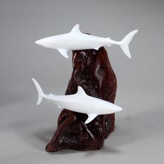 three white plastic sharks sitting on top of a piece of red rock with their mouths open