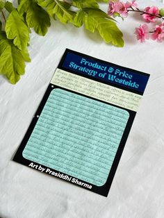 a sheet of paper sitting on top of a table next to pink flowers and green leaves