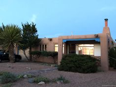 a car is parked in front of a house with cactus trees and bushes around it