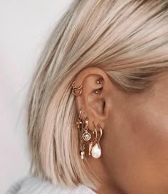 a woman with blonde hair wearing gold ear cuffs and pearl drop earrings on her left ear