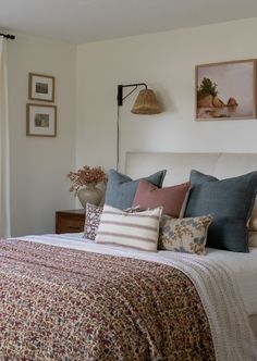 a bed with many pillows on it in a bedroom next to a lamp and window