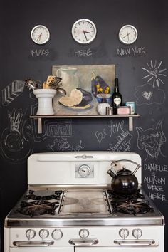 a white stove top oven sitting next to a chalkboard wall with clocks on it