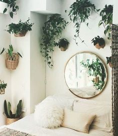 a white bed topped with lots of plants next to a round mirror and potted plants