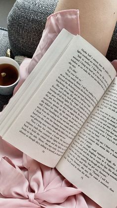 an open book sitting on top of a pink blanket next to a cup of coffee