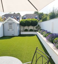 a small backyard with grass and flowers on the lawn, next to a white fence